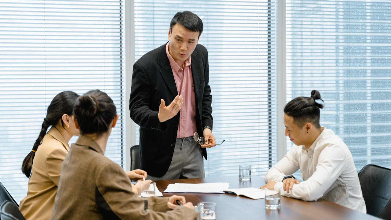 Man standing up and explaining the two classes of stock classes with three individuals sitting at the table with notes and water.